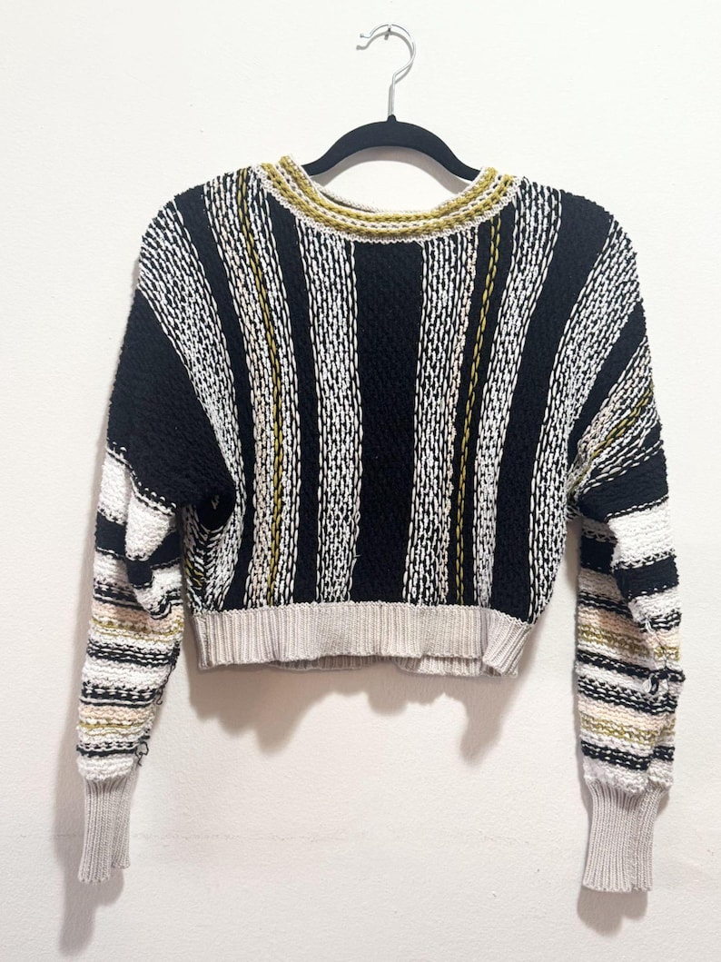 Puede incluir: Un su&eacute;ter corto a rayas con mangas largas. El su&eacute;ter es negro, blanco y verde.
