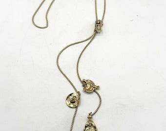 May include: A gold chain necklace with four charms: a cowboy hat, a boot, a horseshoe, and a cowboy figure. The necklace is adjustable in length.