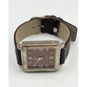 May include: A rectangular watch with a brown face and silver-tone case. The watch has a brown leather band with a silver buckle. The watch face displays the numbers 3, 6, 9, and 12.