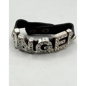 May include: A silver-toned bracelet spelling out "ANGEL" with clear rhinestones. The letters are mounted on a black leather band with snap closures. The bracelet is a fashion accessory.