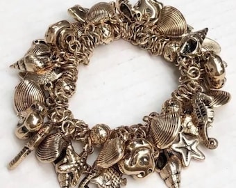 May include: A gold charm bracelet with a variety of sea-themed charms, including seashells, starfish, and seahorses.