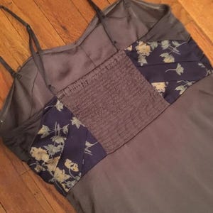 May include: A gray camisole-style dress with thin straps. The bodice features a dark purple, elasticized panel and dark purple panels with a floral pattern. The dress is made of a silky material.