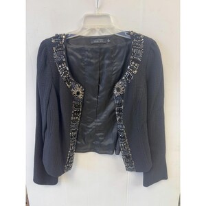 May include: A black blazer with beaded embellishments on the front and sleeves. The blazer has a v-neck and a cropped length. The label "TWIN-SET" is visible on the inside of the blazer.