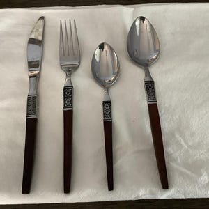 May include: A set of four silver-toned flatware pieces with brown wooden handles. The set includes a knife, fork, and two spoons.