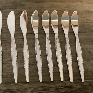 Puede incluir: Ocho cuchillos de mantequilla de plata con un patrón decorativo en el mango.