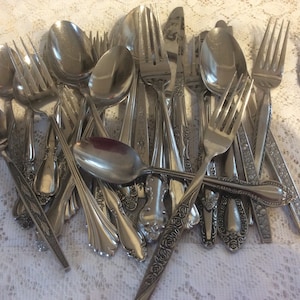 Könnte beinhalten: Ein Stapel silbernes Besteck, darunter Gabeln, Löffel und Messer, mit verzierten Blumendesigns auf den Griffen.