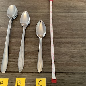May include: Three silver spoons on a wooden surface. The spoons are labeled A, B, and C. The spoon labeled A is a standard teaspoon, the spoon labeled B is a grapefruit spoon, and the spoon labeled C is a citrus spoon.