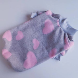May include: A gray fleece dog sweater with a pink heart pattern. The sweater has a high neck and long sleeves.