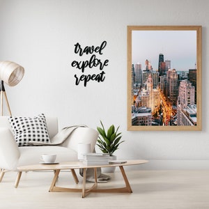 May include: A framed photograph of a city skyline at dusk. The photo shows a cityscape with tall buildings and street lights. The quote "travel explore repeat" is written on the wall above the photo.