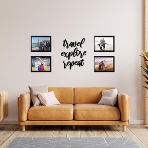 May include: Four black framed photos of people on a wall above a brown leather couch. The photos are arranged in a square shape. The text "travel explore repeat" is written in black script on the wall between the photos.