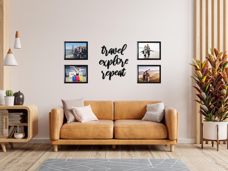 May include: Four black framed photos of people on a wall above a brown leather couch. The photos are arranged in a square shape. The text "travel explore repeat" is written in black script on the wall between the photos.