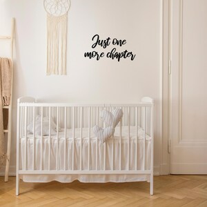 K&ouml;nnte beinhalten: Wei&szlig;es Babybett mit einem wei&szlig;en R&uuml;schenrock und einem schwarzen Wandaufkleber mit der Aufschrift "Just one more chapter".