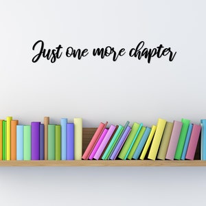 K&ouml;nnte beinhalten: Ein Holzregal mit einer Reihe bunter B&uuml;cher, &uuml;ber dem Regal steht der Text "Just one more chapter" an der Wand.
