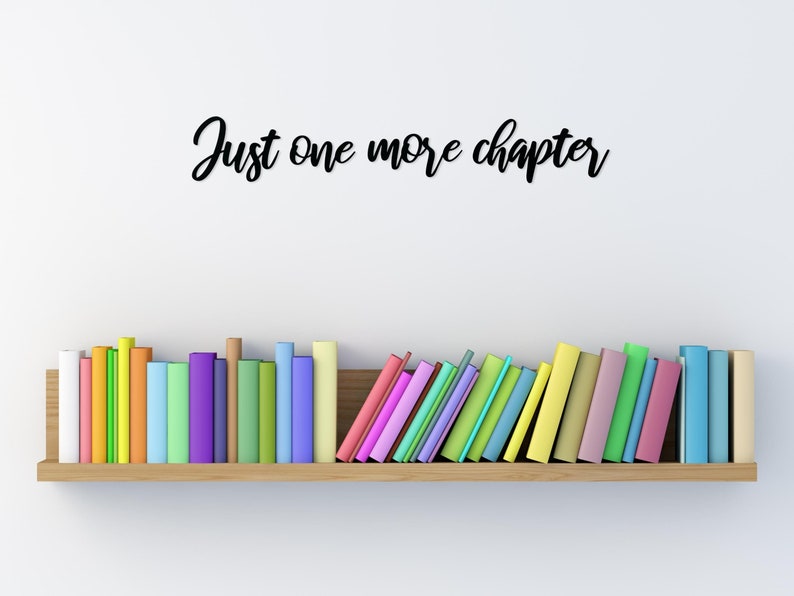 K&ouml;nnte beinhalten: Ein Holzregal mit einer Reihe bunter B&uuml;cher, &uuml;ber dem Regal steht der Text "Just one more chapter" an der Wand.