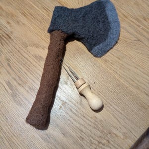 May include: A brown and gray knitted axe with a wooden handle and a metal needle tool.