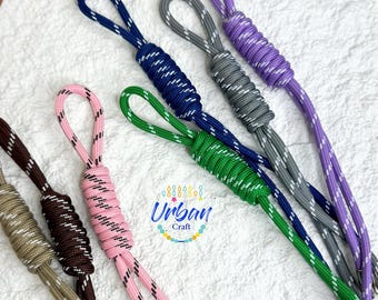 May include: A collection of six colorful rope keychains with white stripes. Each keychain has a loop at the top and a knot in the middle. The keychains are in the colors pink, brown, green, blue, gray, and purple.