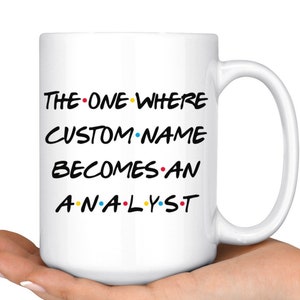 May include: White ceramic mug with a black and white graphic that says "The One Where CUSTOM NAME Becomes An Analyst" with colorful dots.