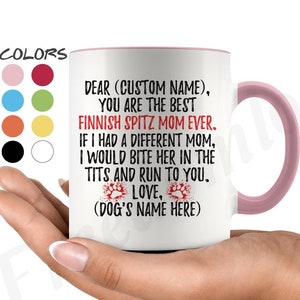 Może przedstawiać: Biały ceramiczny kubek z różowym wnętrzem i uchwytem. Kubek zawiera tekst w kolorze czarnym i czerwonym, w tym "Finnish Spitz Mom Ever". Kubek jest trzymany w dłoni, widoczna jest paleta kolorów.