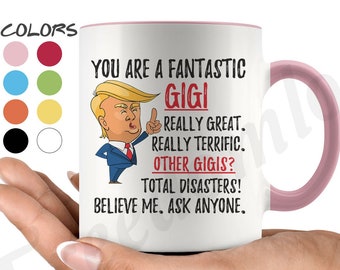 May include: White ceramic mug with a pink rim. The mug features a cartoon image of a man with a red tie and a white shirt. The text on the mug reads "You are a fantastic Gigi. Really great. Really terrific. Other Gigis? Total disasters! Believe me. Ask anyone."