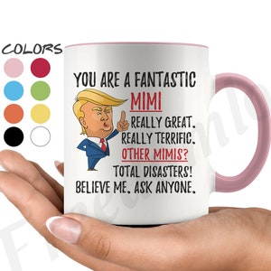 Puede incluir: Taza de cerámica blanca con borde y asa de color rosa. La taza presenta una imagen de dibujos animados de un hombre con corbata roja y un dedo apuntando. El texto en la taza dice "You are a fantastic Mimi. Really great. Really terrific. Other Mimis? Total disasters! Believe me. Ask anyone."