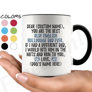 May include: White ceramic coffee mug with a black handle. The mug has a blue and white text design that reads "Dear (Custom Name), You are the best Olde English Bulldogge Dad Ever. If I had a different Dad, I would bite him in the nuts and run to you. Love, (Dog's Name Here)"