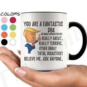 Könnte beinhalten: Eine weiße Keramik-Kaffeetasse mit schwarzem Henkel. Die Tasse zeigt ein Cartoon-Bild eines Mannes mit roter Krawatte und schwarzem Anzug. Der Text auf der Tasse lautet "You are a fantastic DBA (Database Administrator) Really great. Really terrific. Other DBAs? Total disasters! Believe me. Ask anyone."