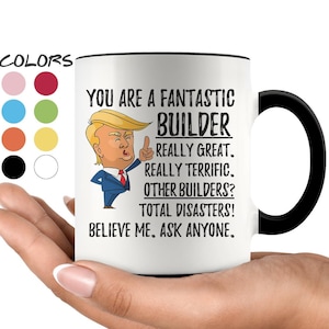 May include: White ceramic coffee mug with a black rim and handle. The mug features a cartoon image of a man with a red tie and a black suit. The text on the mug reads "You are a fantastic builder. Really great. Really terrific. Other builders? Total disasters! Believe me. Ask anyone."