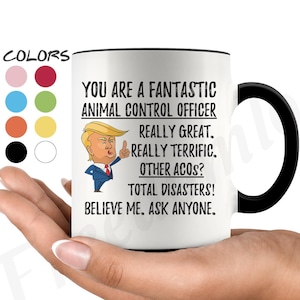 Könnte beinhalten: Eine weiße Keramik-Kaffeetasse mit schwarzem Henkel. Die Tasse hat einen schwarzen Rand und zeigt ein Cartoon-Bild eines Mannes mit roter Krawatte und einem Daumen hoch. Der Text auf der Tasse lautet "You are a fantastic animal control officer. Really great. Really terrific. Other ACOS? Total disasters! Believe me. Ask anyone."