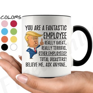 May include: White ceramic coffee mug with a black rim and handle. The mug features a cartoon image of a man with blonde hair and a red tie. The text on the mug reads "You are a fantastic employee. Really great. Really terrific. Other employees? Total disasters! Believe me. Ask anyone."