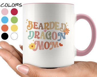 May include: White ceramic mug with a pink rim and handle. The mug features a colorful graphic that says "Bearded Dragon Mom" with flowers and hearts.