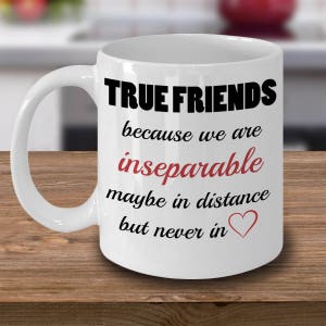 Pode incluir: Caneca de café de cerâmica branca com texto preto que diz "TRUE FRIENDS because we are inseparable maybe in distance but never in" com um coração vermelho.
