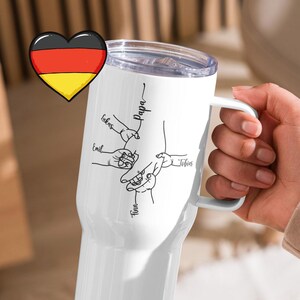 Pode incluir: Caneca de viagem branca com alça, com um desenho de mãos e nomes. Os nomes incluem "Papa", "Lukas", "Emil", "Tinn" e "Jefin". Um coração com a bandeira alemã está no canto superior esquerdo. A caneca é segurada por uma pessoa.