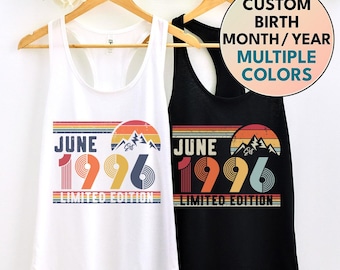 May include: White and black tank tops with a retro design. Each tank top features the word "JUNE" above the year "1996" with a mountain graphic. The text "LIMITED EDITION" is below. The design includes multiple colors.