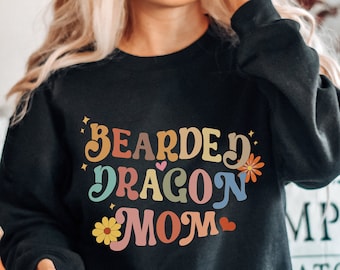 Op de afbeelding: Zwart sweatshirt met de tekst "Bearded Dragon Mom" in kleurrijke retro letters met bloemen en harten.