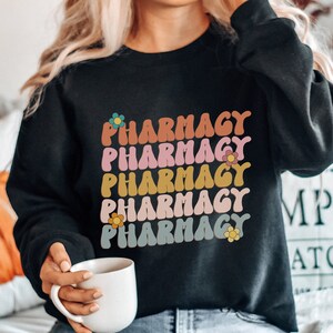 May include: A black sweatshirt with the word "Pharmacy" repeated five times in a rainbow of colors with a flower graphic next to each word.