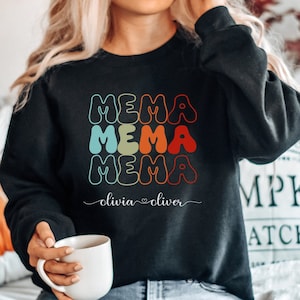 Könnte beinhalten: Schwarzer Pullover mit einer regenbogenfarbenen Grafik, auf der dreimal "MEMA" steht. Der Text "olivia♡oliver" steht unter der Grafik.