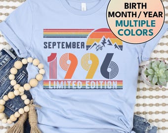 May include: A light blue t-shirt featuring a graphic with the text SEPTEMBER EST 1996 LIMITED EDITION, a mountain silhouette, and a sunset design in red, orange, and yellow. A circular badge reads CUSTOM BIRTH MONTH / YEAR MULTIPLE COLORS.
