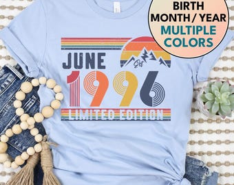 May include: Light blue t-shirt with the text "JUNE 1996 LIMITED EDITION" in a retro design. The design includes a mountain graphic and a rainbow color scheme. The shirt also has a circular graphic that says "CUSTOM BIRTH MONTH/YEAR MULTIPLE COLORS".