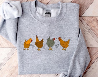 May include: A gray sweatshirt with a graphic of five chickens in a line. The chickens are brown and yellow with black eyes and beaks. The chickens are facing forward and have their wings slightly raised. The sweatshirt has a crew neck and long sleeves.