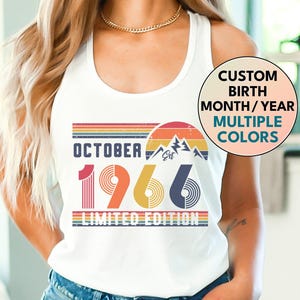 May include: A white tank top featuring a retro-style graphic with the text OCTOBER 1966 LIMITED EDITION. The design includes a sunset, mountain silhouettes, and horizontal stripes in muted orange, yellow, and blue tones. A circular badge reads CUSTOM BIRTH MONTH/YEAR MULTIPLE COLORS.