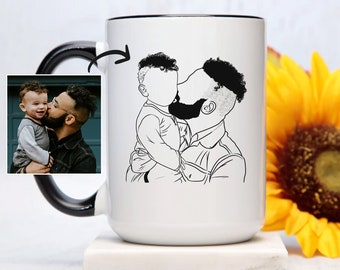 Könnte beinhalten: Eine weiße Keramiktasse mit schwarzem Henkel und schwarzem Rand. Die Tasse zeigt eine Schwarzweiß-Zeichnung eines Vaters und seines Sohnes, die sich umarmen. Der Vater hält den Sohn in seinen Armen. Der Sohn schaut zu seinem Vater auf. Die Tasse steht auf einer weißen Oberfläche.