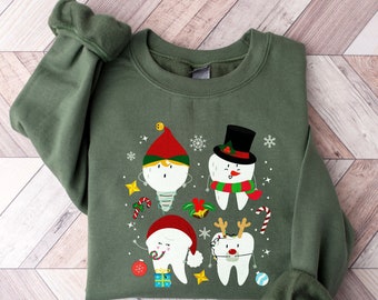 以下が含まれることがあります： 緑色のスウェットシャツ。クリスマスをテーマにした4つの漫画の歯のデザイン。1つはエルフ、もう1つは雪だるま、3つ目はサンタ、最後はトナカイ。デザインには、キャンディケインとお祝いのオーナメントが含まれています。