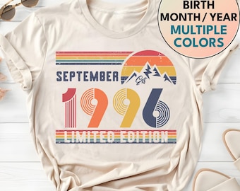 May include: A cream-colored t-shirt featuring a graphic with the text SEPTEMBER 1996 LIMITED EDITION. The design includes a sunset, mountain silhouette, and horizontal stripes in red, orange, yellow, and blue. A circular badge reads CUSTOM BIRTH MONTH/YEAR MULTIPLE COLORS.