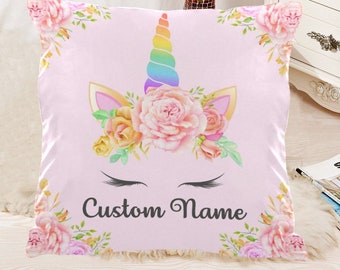 May include: Pink pillow with a unicorn face and floral design. The unicorn has a rainbow horn and closed eyes. The text "Custom Name" is printed below the unicorn.
