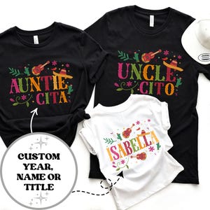 May include: Three black t-shirts with colorful text and graphics. The shirts say "Auntie Cita", "Uncle Cito", and "Isabella".