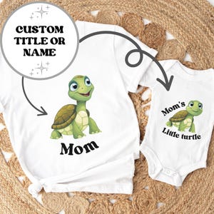 May include: Two white t-shirts with a green turtle graphic. The larger shirt says "Mom" and the smaller shirt says "Mom's Little Turtle".