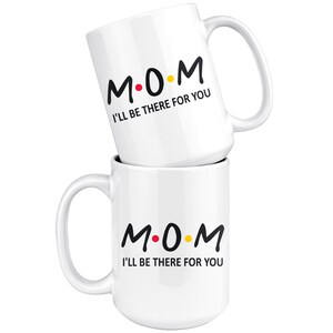 May include: Two white ceramic mugs with black text that reads "M.O.M. I'll be there for you". The "O" in "MOM" is a red dot and the "M" is a yellow dot.
