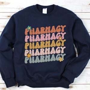 May include: Navy blue sweatshirt with the word "Pharmacy" repeated five times in a retro font with colorful flowers.