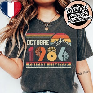 Op de afbeelding: Een antracietgrijs t-shirt met een retro-stijl afbeelding met de tekst OCTOBRE 1986 EDITION LIMITEE. Het ontwerp bevat een zonsondergang boven bergtoppen in oranje, gele en blauwe tinten, met concentrische cirkelpatronen in de cijfers.