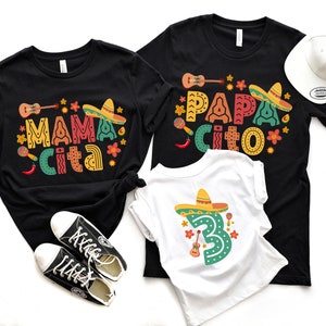 May include: Three black t-shirts with colorful text and graphics. The shirts say "Mama Cita", "Papa Cita", and "3" with a sombrero.